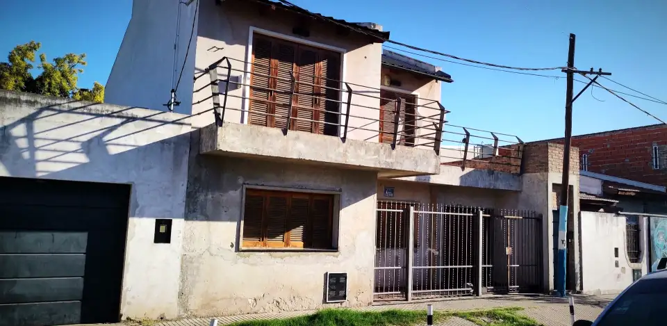 A two-storey house with shutters and an iron balcony under a hard blue sky, in the Rosario neighbourhood where Messi grew up.