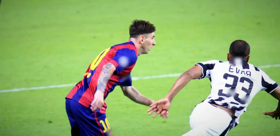 Messi in Barcelona colours chasing alongside a Juventus player with EVRA 33 on his shirt, on open green. 2015 Champions League final, Berlin. Marks blurred in the film.