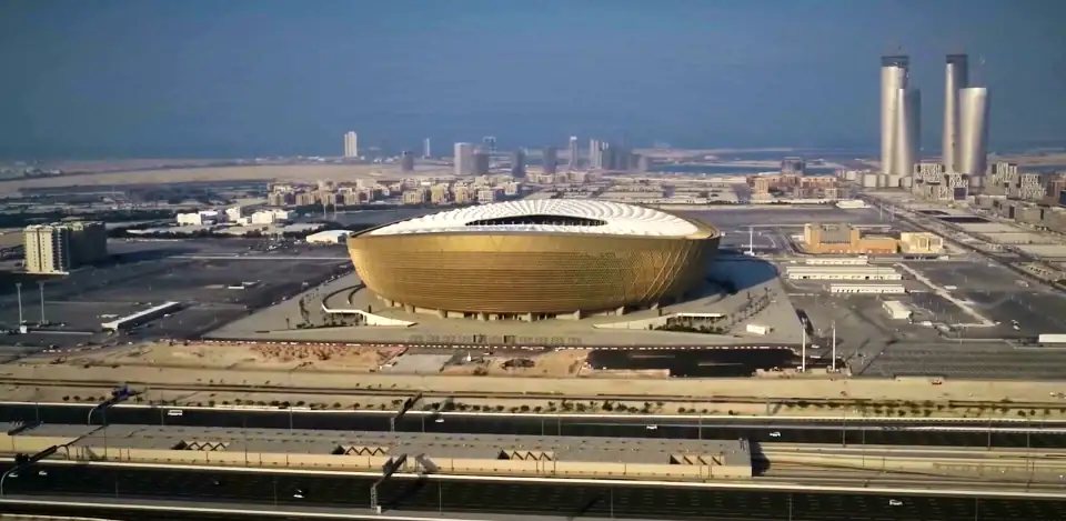 Aerial view of Lusail Stadium, Qatar, in daylight haze: a gold bowl in flat land, with towers on the horizon.