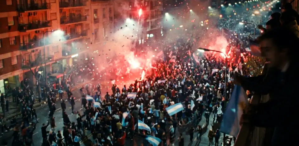 A huge street crowd from above at night, red flares and smoke between apartment blocks.