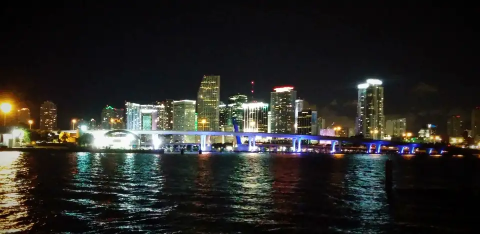 The Miami skyline at night across dark water, with coloured reflections.
