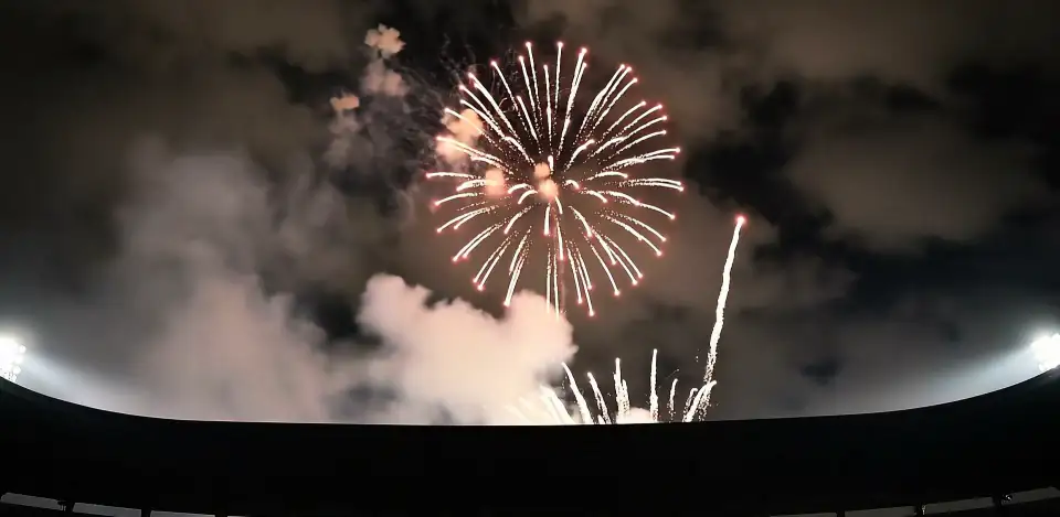 Fireworks and white smoke above the dark rim of a stadium.