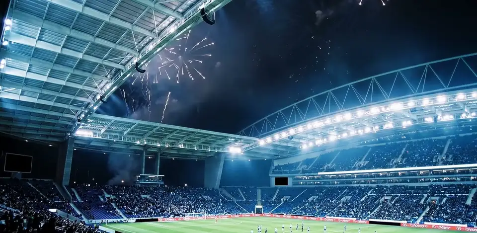 Smoke drifting under the roof of a floodlit blue stadium at night.